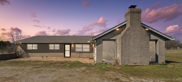 view of front facade featuring a patio, brick siding, a front yard, and a chimney