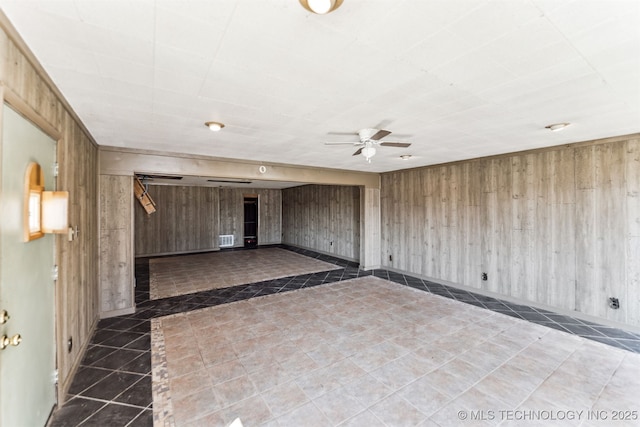 tiled empty room featuring wooden walls, visible vents, a ceiling fan, and a barn door