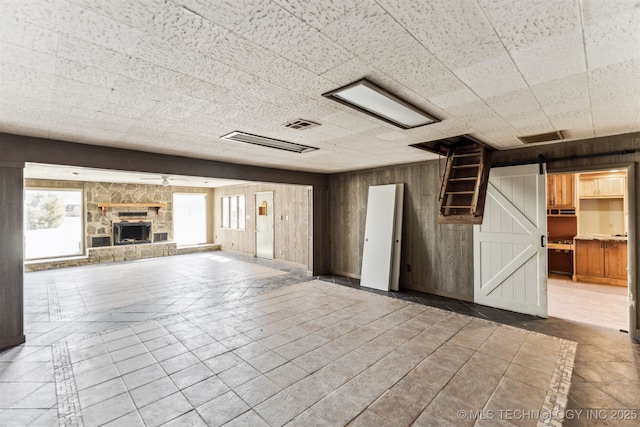 unfurnished living room featuring visible vents, a barn door, wood walls, a fireplace, and tile patterned flooring