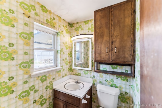 bathroom featuring toilet, wallpapered walls, and vanity