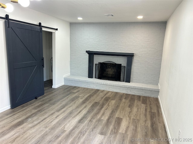 unfurnished living room featuring hardwood / wood-style flooring, a barn door, and a brick fireplace