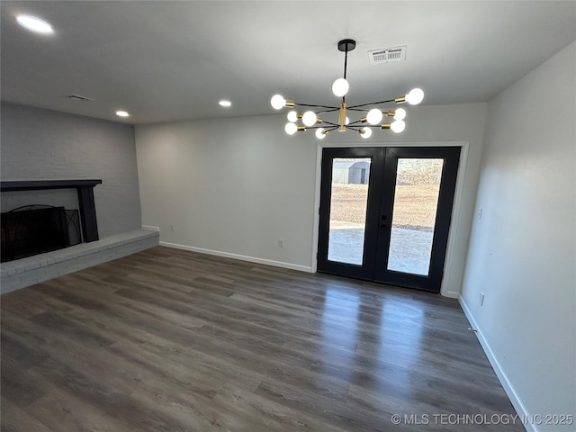 unfurnished living room with french doors, dark hardwood / wood-style floors, a chandelier, and a brick fireplace