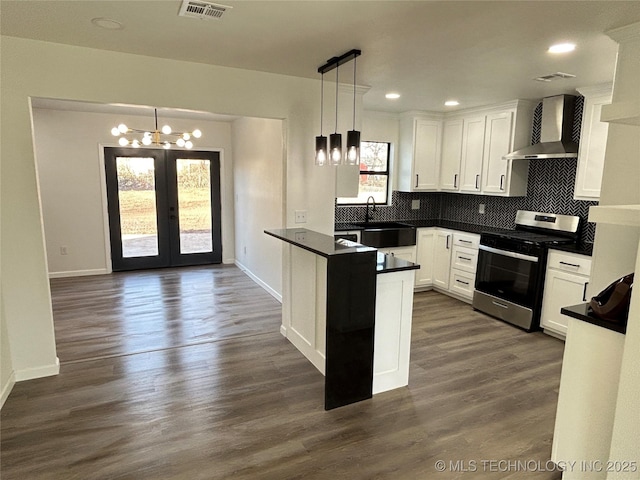 kitchen featuring gas range, wall chimney range hood, white cabinets, and decorative light fixtures