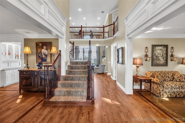 staircase with wood-type flooring, ornamental molding, and a high ceiling