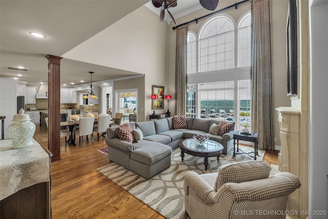 living room featuring crown molding, hardwood / wood-style flooring, decorative columns, and a high ceiling