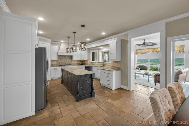 kitchen featuring white cabinetry, hanging light fixtures, appliances with stainless steel finishes, a kitchen island, and light stone countertops