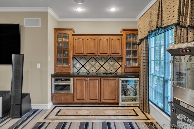 kitchen featuring sink, beverage cooler, decorative backsplash, ornamental molding, and stainless steel oven