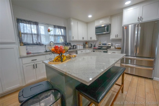 kitchen with a breakfast bar, light stone counters, tasteful backsplash, stainless steel appliances, and white cabinets