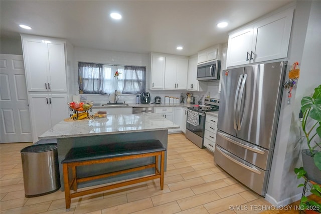 kitchen with sink, stainless steel appliances, a kitchen breakfast bar, white cabinets, and a kitchen island