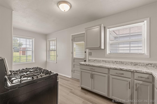 kitchen featuring gray cabinets, gas stove, light wood-type flooring, and light stone counters