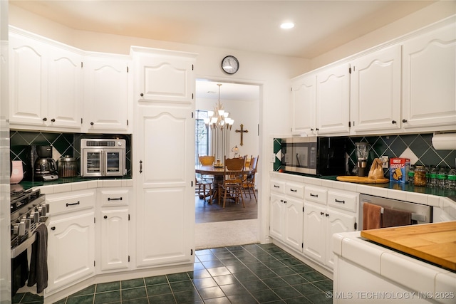 kitchen with appliances with stainless steel finishes, white cabinetry, tasteful backsplash, tile counters, and dark tile patterned flooring