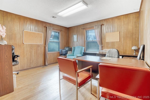 office with wood walls, a textured ceiling, and light wood-type flooring