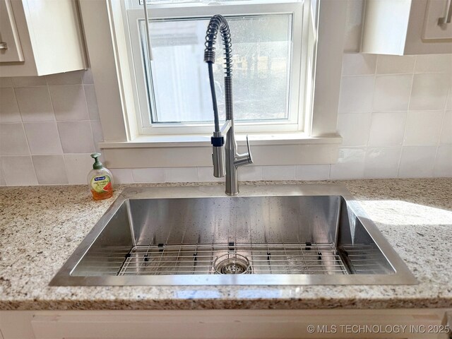 details with tasteful backsplash, light stone countertops, sink, and white cabinets