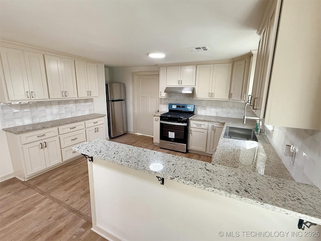 kitchen with sink, light hardwood / wood-style floors, kitchen peninsula, stainless steel appliances, and light stone countertops