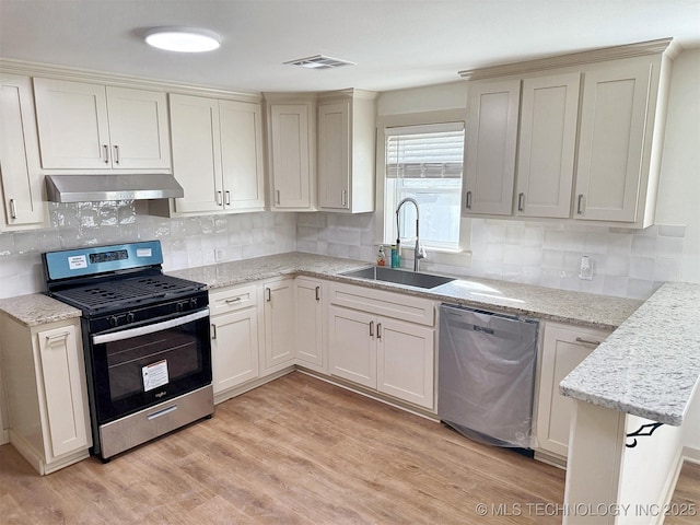 kitchen with sink, light stone counters, appliances with stainless steel finishes, light hardwood / wood-style floors, and decorative backsplash