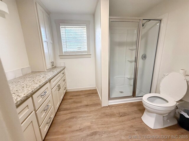 bathroom featuring hardwood / wood-style flooring, vanity, a shower with door, and toilet