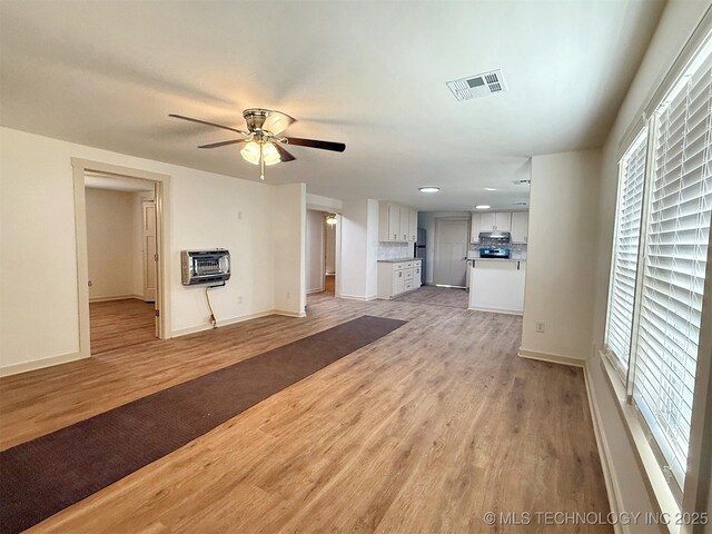 unfurnished living room featuring ceiling fan, heating unit, and light wood-type flooring