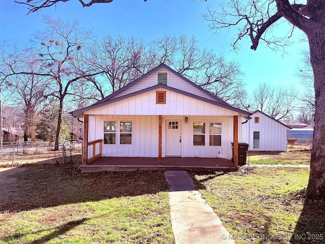 bungalow-style home featuring covered porch, board and batten siding, a front lawn, and fence