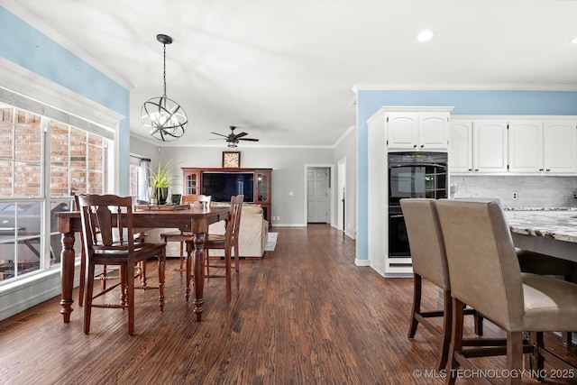 dining area featuring dark wood-type flooring, ornamental molding, and ceiling fan with notable chandelier