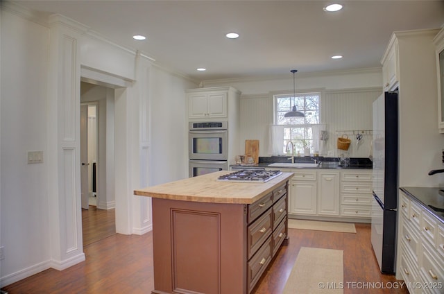 kitchen with butcher block counters, a center island, pendant lighting, stainless steel appliances, and white cabinets