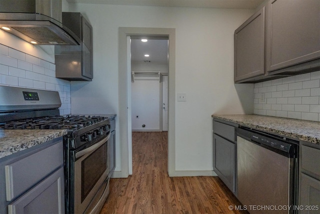 kitchen with gray cabinets, appliances with stainless steel finishes, ventilation hood, light stone countertops, and wood-type flooring