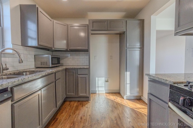 kitchen featuring sink, light stone counters, light wood-type flooring, appliances with stainless steel finishes, and decorative backsplash