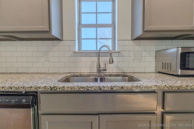 kitchen featuring sink, light stone counters, appliances with stainless steel finishes, gray cabinets, and backsplash