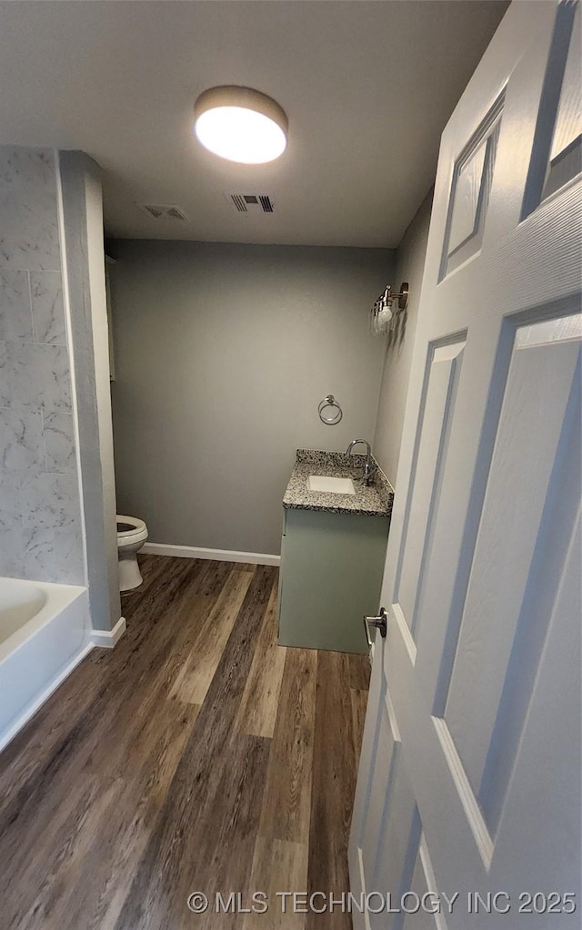 bathroom with wood-type flooring, toilet, vanity, and a tub