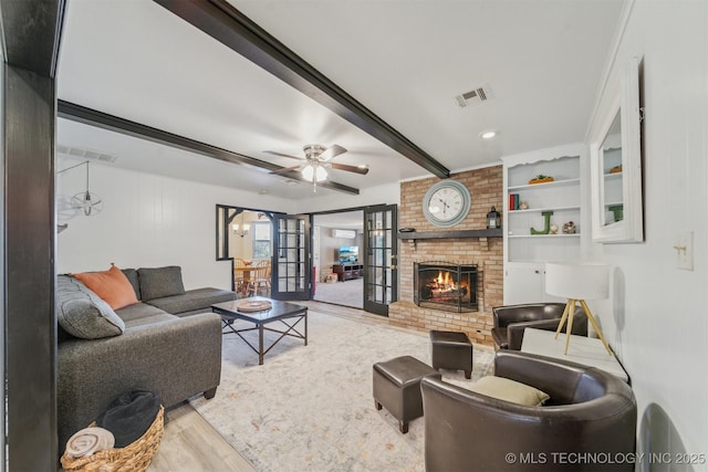 living room featuring french doors, a brick fireplace, light wood-type flooring, beamed ceiling, and ceiling fan