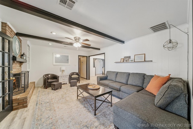 living room featuring ceiling fan, beam ceiling, a brick fireplace, and light hardwood / wood-style flooring