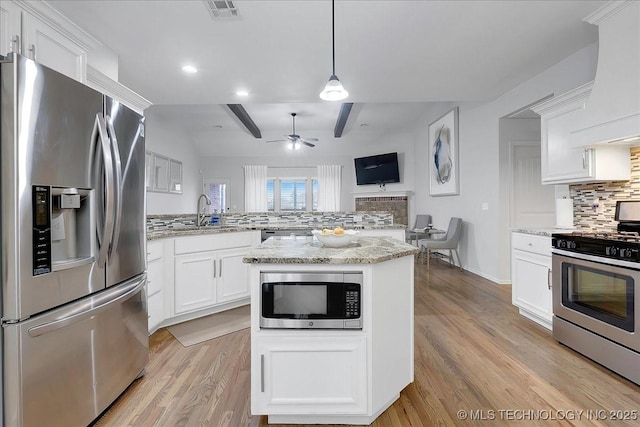 kitchen featuring appliances with stainless steel finishes, decorative light fixtures, white cabinets, backsplash, and light stone countertops