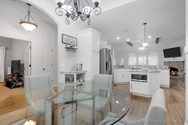 dining area featuring ceiling fan, sink, a fireplace, and light hardwood / wood-style floors