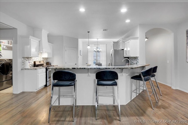 kitchen featuring light stone countertops, premium range hood, appliances with stainless steel finishes, and washer / clothes dryer