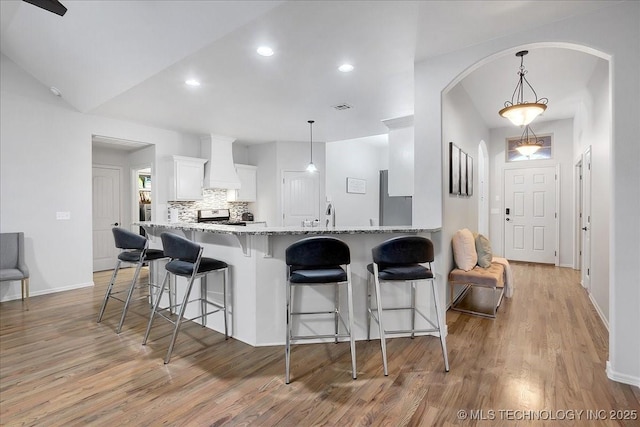 kitchen featuring pendant lighting, light stone countertops, custom exhaust hood, and white cabinets