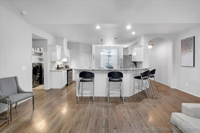 kitchen featuring washer and clothes dryer, appliances with stainless steel finishes, white cabinetry, light stone counters, and kitchen peninsula