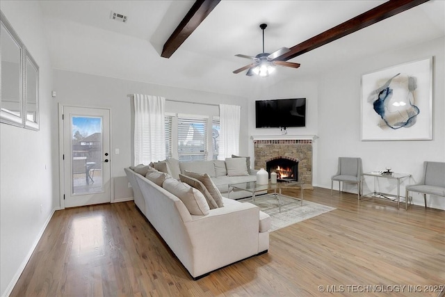 living room featuring a stone fireplace, light hardwood / wood-style flooring, lofted ceiling with beams, and ceiling fan