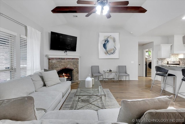 living room with hardwood / wood-style flooring, ceiling fan, a fireplace, lofted ceiling with beams, and washer / dryer