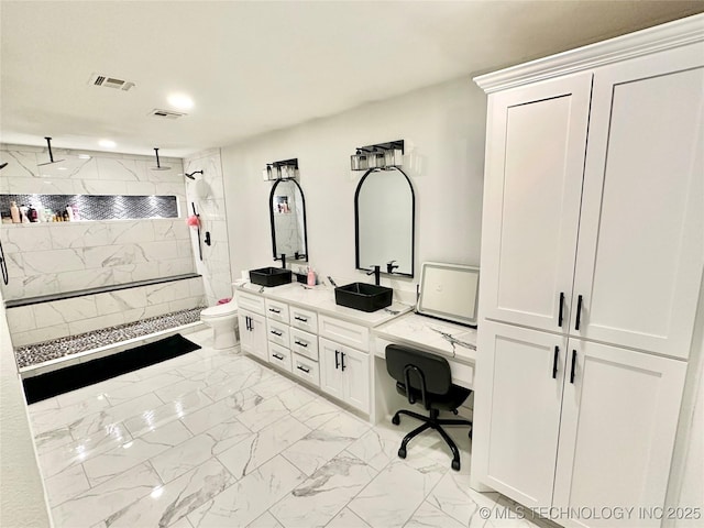 bathroom with a tile shower, vanity, and toilet