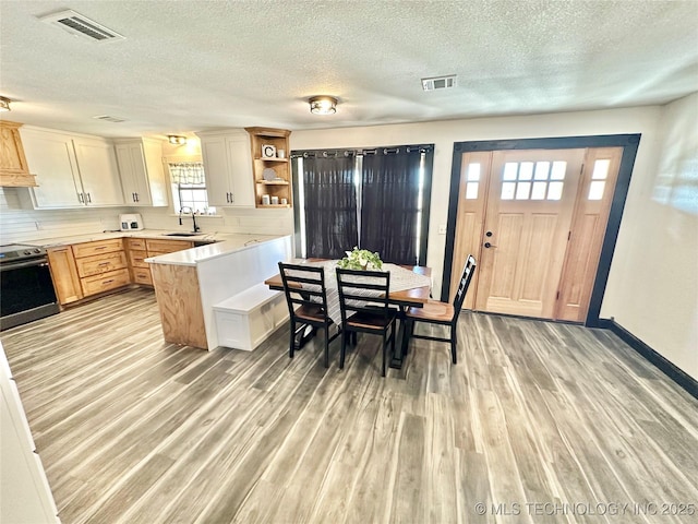 kitchen with light brown cabinetry, white cabinetry, stainless steel electric stove, and light hardwood / wood-style floors