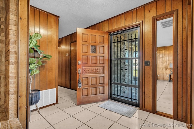 tiled entryway with a textured ceiling and wood walls