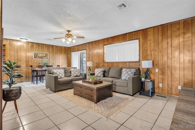 tiled living room with ceiling fan, wooden walls, and a textured ceiling