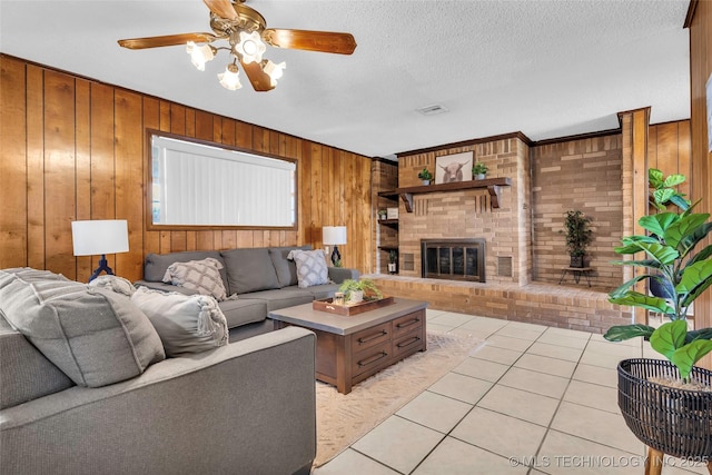 tiled living room with built in features, wooden walls, a fireplace, ceiling fan, and a textured ceiling