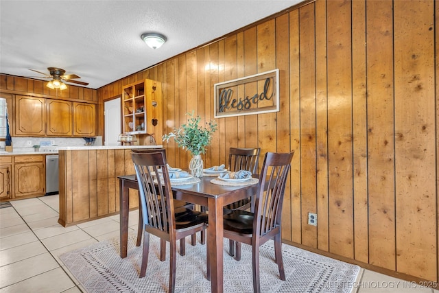 dining room with ceiling fan, wooden walls, a textured ceiling, and light tile patterned floors