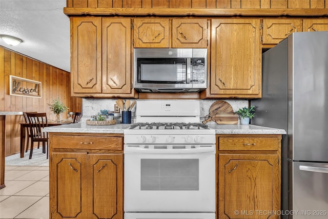 kitchen with light tile patterned flooring, appliances with stainless steel finishes, decorative backsplash, and wood walls