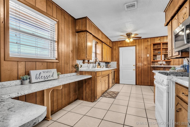 kitchen with white range with gas cooktop, sink, wood walls, and light tile patterned floors