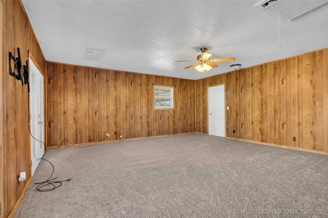 carpeted empty room featuring ceiling fan, wooden walls, and a textured ceiling