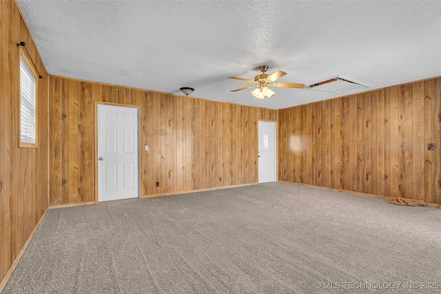 spare room with ceiling fan, wooden walls, carpet, and a textured ceiling