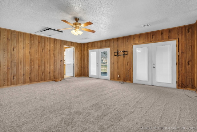 unfurnished living room featuring carpet flooring, wood walls, ceiling fan, and french doors