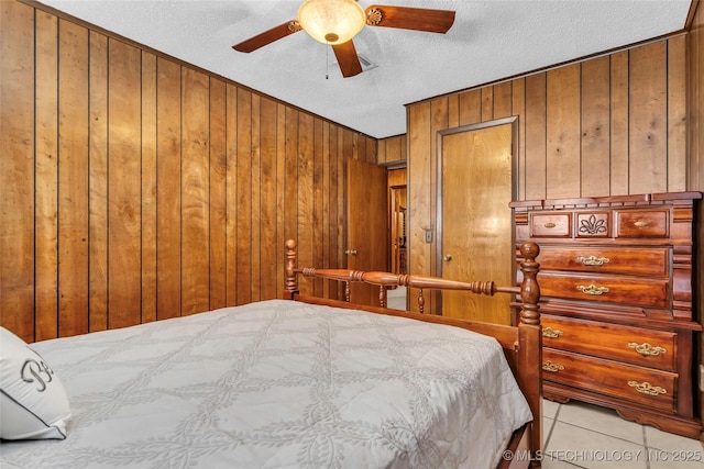 bedroom featuring ceiling fan, light tile patterned floors, a textured ceiling, and wooden walls