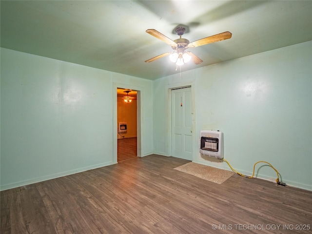 unfurnished room featuring wood-type flooring, a wood stove, heating unit, and ceiling fan